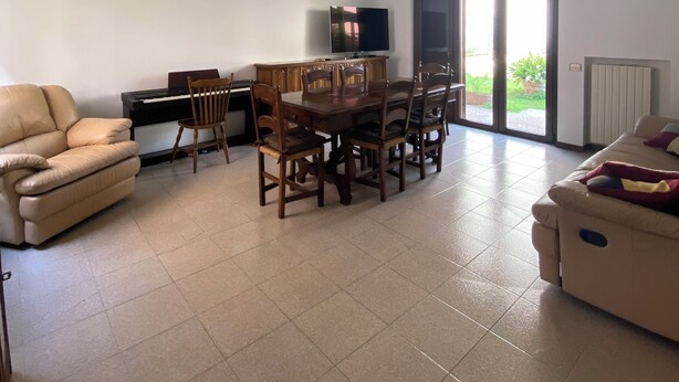 Een ruime woonkamer met een eettafel, stoelen, een bank, een piano en een televisie.