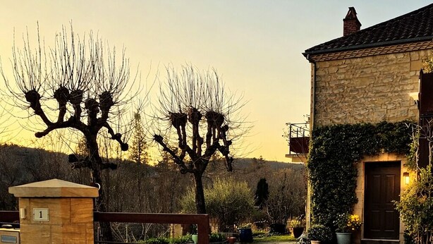 Un bâtiment en pierre avec un portail en bois, une pelouse bien entretenue et un arbre aux branches nues.