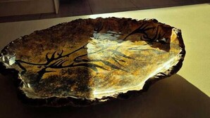 Une table ornée d’un élément décoratif en verre qui reflète la lumière du soleil, une fenêtre avec des rideaux et une vue sur les arbres à l’extérieur.