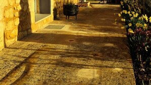 Un bâtiment en pierre doté d’un balcon, d’une porte et d’un chemin menant à un jardin fleuri.