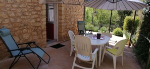 Une terrasse dallée de pierres, avec une table ronde et quatre chaises, un parasol et une porte donnant sur un espace intérieur.