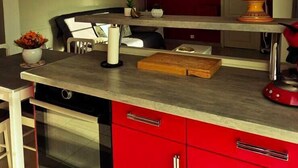 Une cuisine moderne avec des meubles de rangement rouges, un four encastré et un plan de travail sur lequel sont disposés divers objets.