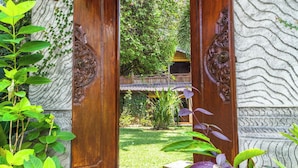 A wooden door with intricate carvings, leading to a garden with a stone wall and a traditional tiled structure. - Villa Seahorse, Bali - Lovina Beach Poolvilla, 2BR Joglo! (Buleleng)