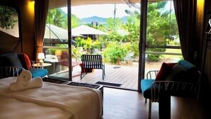 A hotel room with a large sliding glass door leading to an outdoor deck with a table and chairs, a bed with a pillow, and a small table with a lamp. - King tent 5 Nelly bay (Nelly Bay)