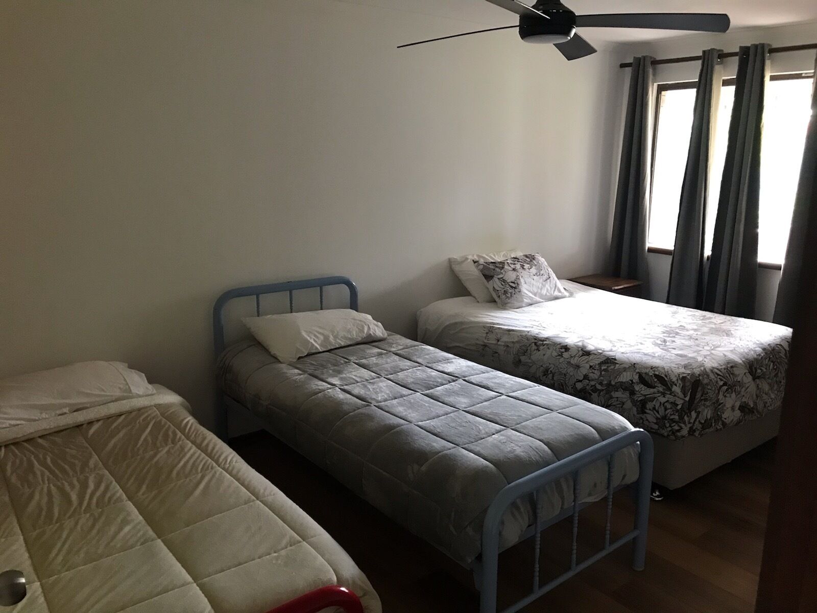 Una habitación con dos camas individuales, ventilador de techo y ventana con cortinas.