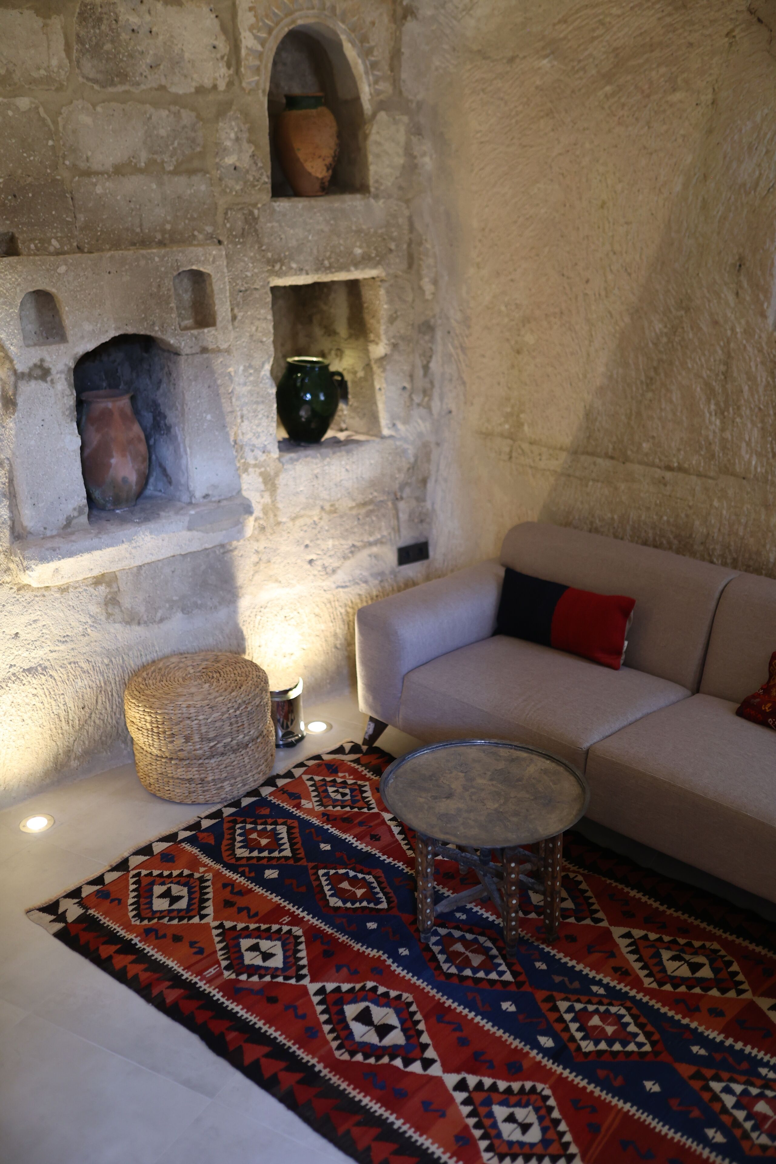 Una habitación con pared de piedra, un sofá color beige, un tapete estampado y una mesita redonda.