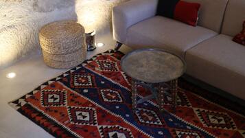 Una habitación con pared de piedra, un sofá color beige, un tapete estampado y una mesita redonda.