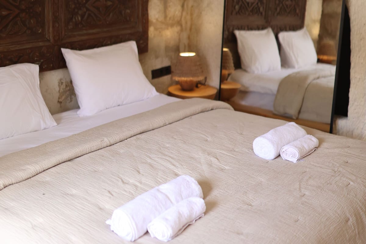 Une chambre à coucher avec un grand lit, une tête de lit en bois, une table de chevet avec une lampe et un miroir qui reflète le lit.