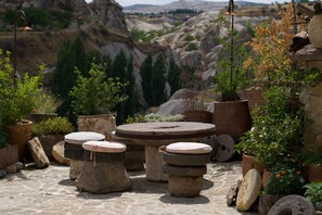 A rustic outdoor seating area with stone tables and benches, surrounded by potted plants and a mountainous backdrop. - Potamia Cave Suites (Ürgüp)