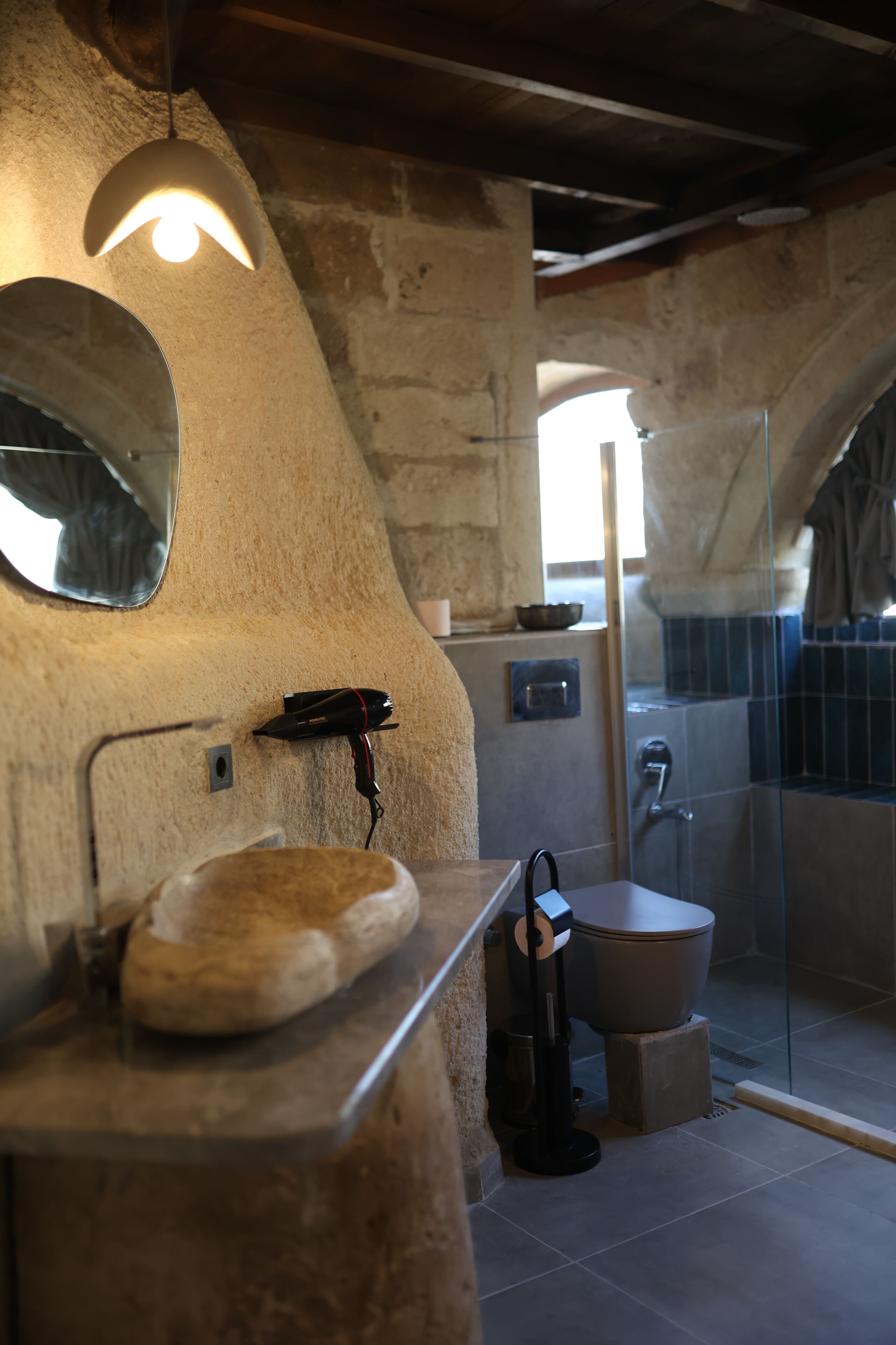 Ein rustikales Badezimmer mit einem Steinkonfession, einem Spiegel, einer Dusche und einer Toilette.