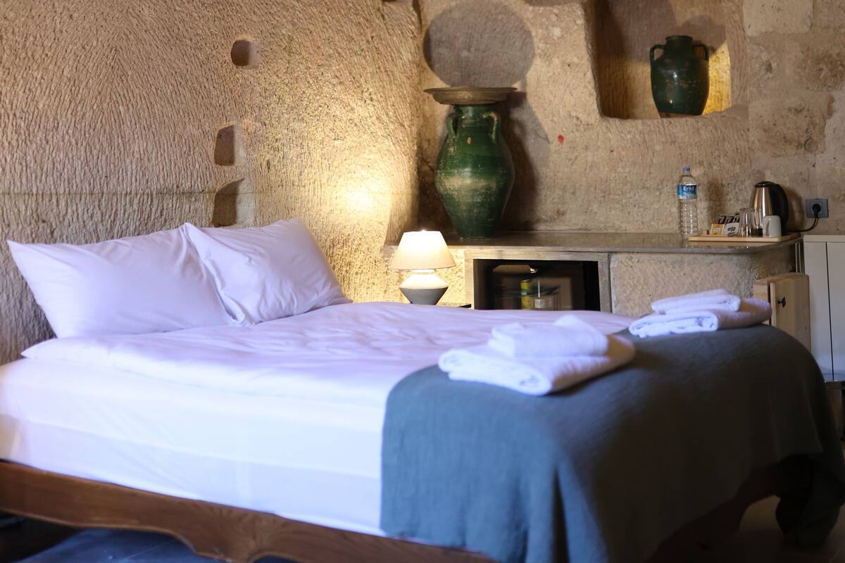 Une pièce rustique avec un lit, un vase vert, un meuble en bois et un mur en pierre.