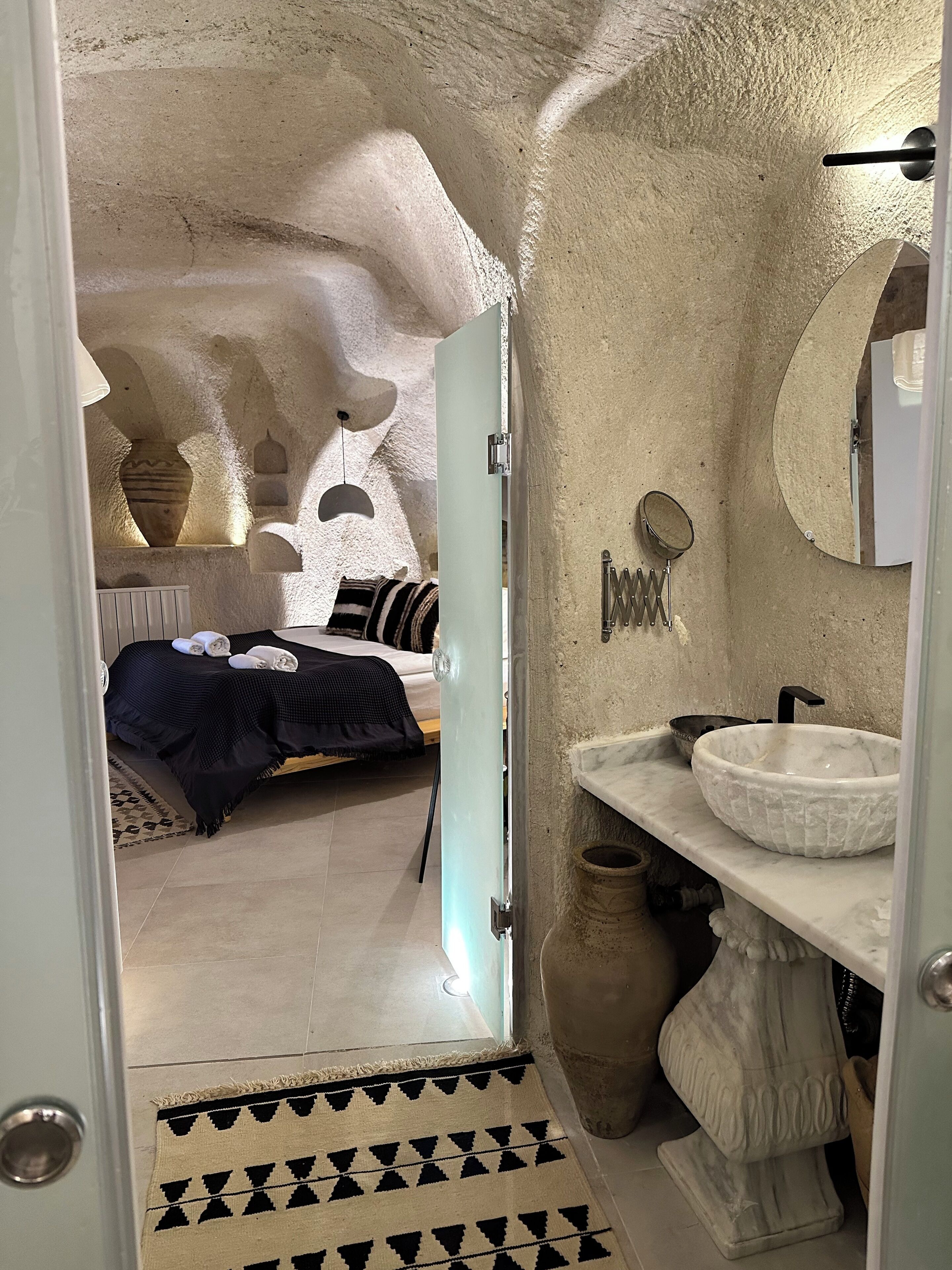 Une chambre avec un lit, une table de chevet, une lampe suspendue et une vue sur la salle de bain.