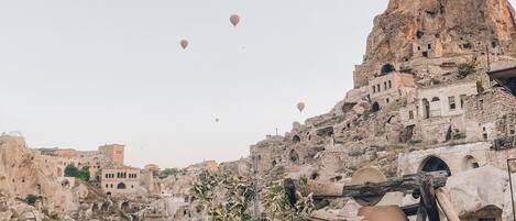 A hot air balloon with "Premium Caves" written on it flying over a rocky landscape with traditional stone buildings.