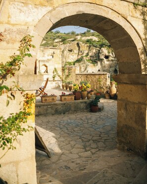 An outdoor courtyard with stone flooring, a wooden chair, and potted plants. - Potamia Cave Suites (Ürgüp)