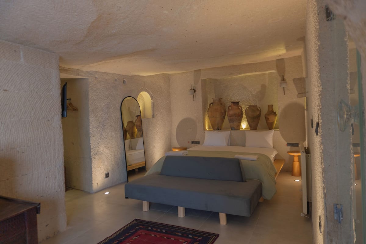 Une chambre avec un lit, un canapé et un grand miroir. Des vases décoratifs sont accrochés au mur.