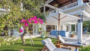 A covered outdoor seating area with lounge chairs and a pergola with pink bougainvillea.