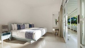 A modern bedroom with a large bed, a nightstand, and a view of a balcony with plants.