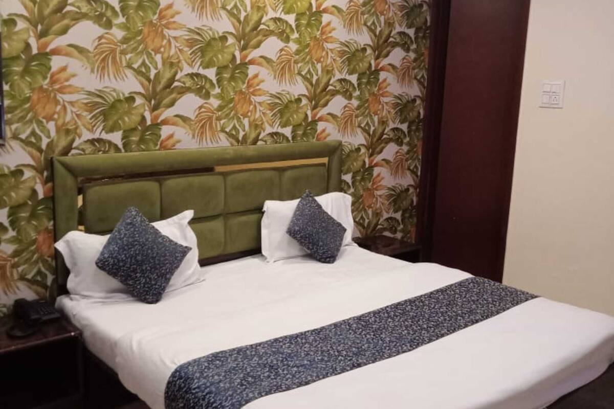 A hotel room with a bed, a nightstand, a wall with tropical wallpaper, and a door.