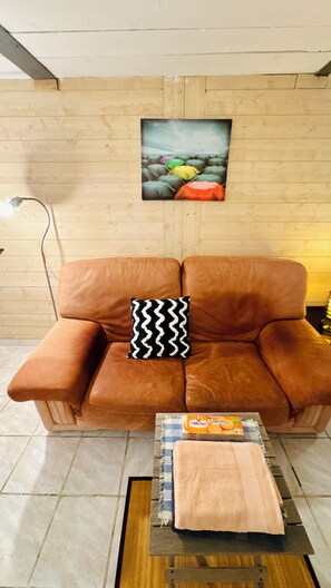 A brown leather sofa with a black and white patterned pillow, a painting on the wall, and a box of S'Michel Galettes on a small table. - Peaceful Studio 35m² + Private Sunny Courtyard | Prime Location in Marseille 6th (Marseille)
