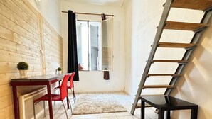 Un espacio habitable compacto con una escalera, un comedor con sillas rojas y un sofá.