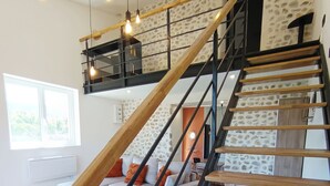 A modern staircase with wooden steps and black railings, leading to a living area with a sofa and a view of the outdoors.