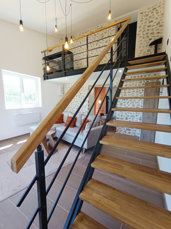 A modern staircase with wooden steps and black railings, leading to a living area with a sofa and a view of the outdoors.