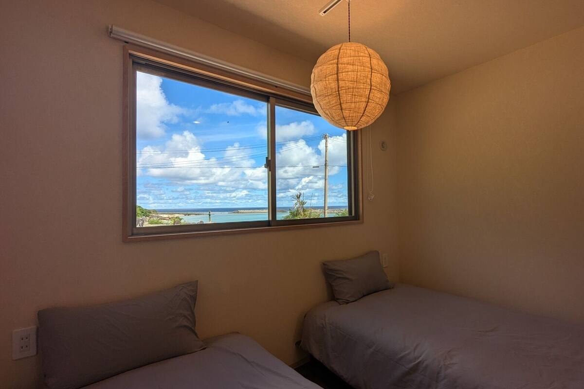 A room with two beds, a large window, and a hanging light fixture.