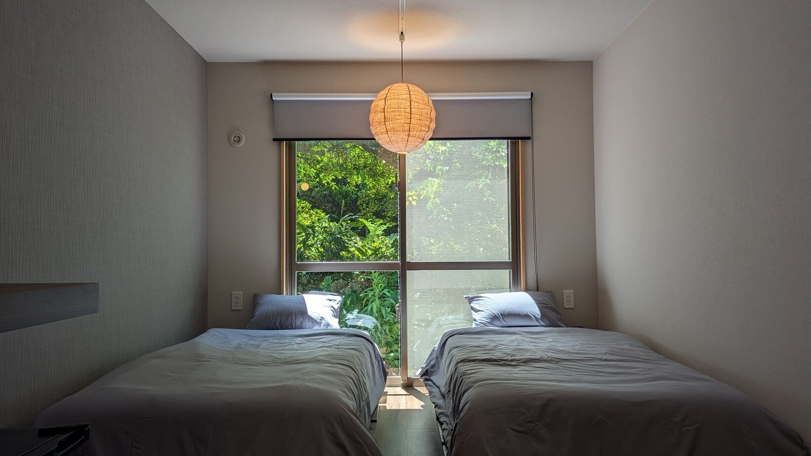 A bedroom with two beds, a large window, and a hanging light fixture.