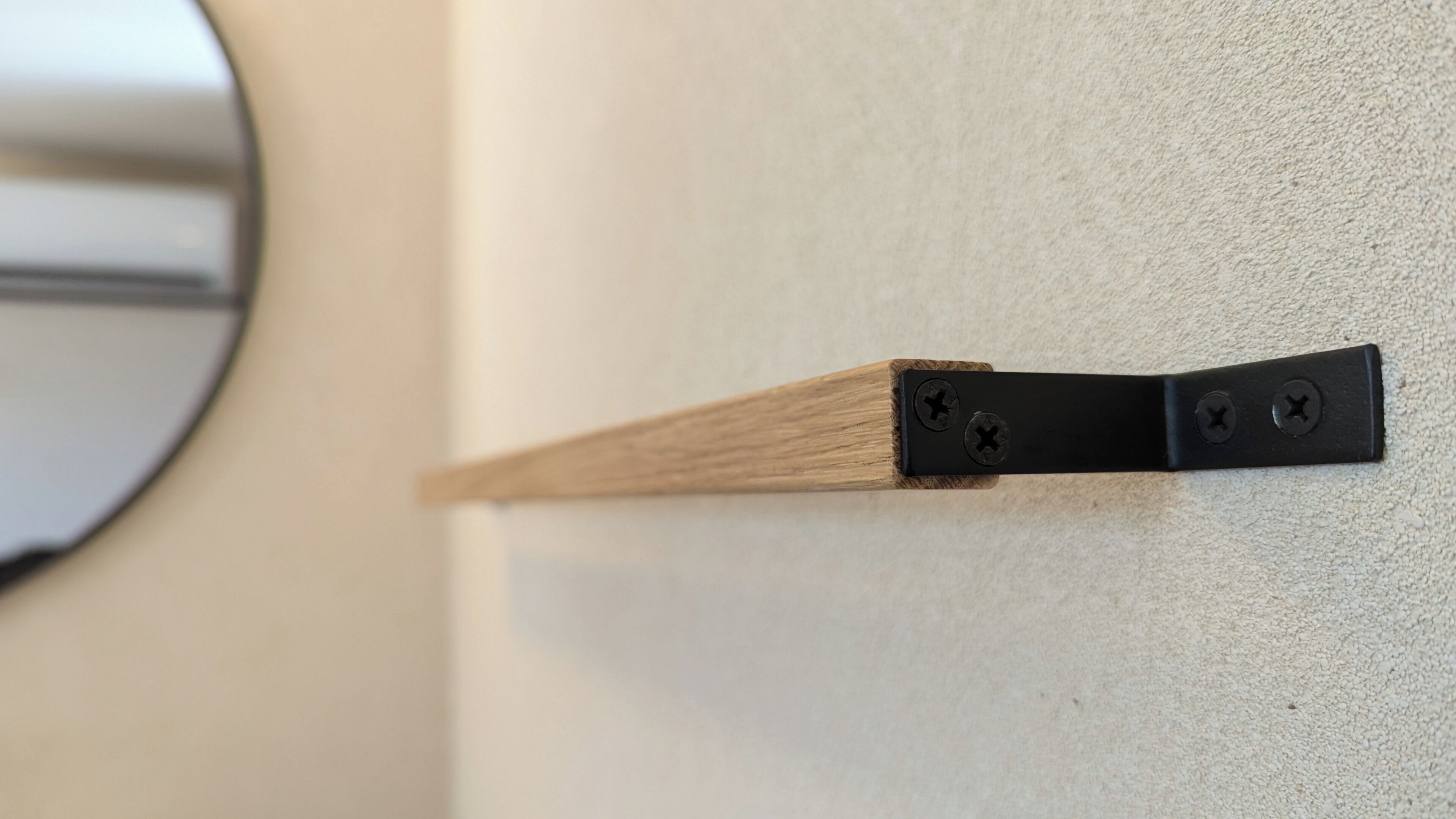 Un tope de madera con un soporte de metal negro, dos tornillos y un espejo circular en una pared con textura.