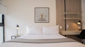 Ein Hotelzimmer mit einem Bett, einem Nachttisch mit Lampe, einem Wandregal und einem gerahmten Bild über dem Bett.