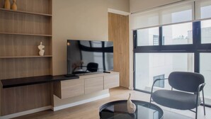 Ein modernes Wohnzimmer mit Flachbildfernseher, Holzbögen, einem Glastisch und einem bequemen Sessel.