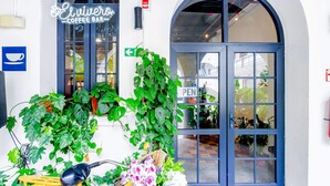 Un café avec une enseigne, une porte sur laquelle est affiché le mot « OUVERT », et un vélo avec un panier rempli de fleurs.
