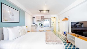 Une chambre d’h ôtel moderne dotée d’un grand lit, d’une télévision, d’une kitchenette et d’une salle de bain visible à travers une porte ouverte.
