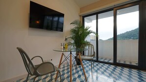 A room with a glass table, two chairs, a potted plant, and a large window with a view of a hill. - w* | Comfortable Loft in Santa Ana (Panamá)