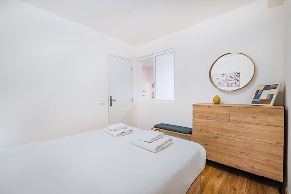 A bedroom with a bed, a wooden dresser, a bench, a door, and a window. - Pilar Apartment by Dreamplaces (Albufeira)