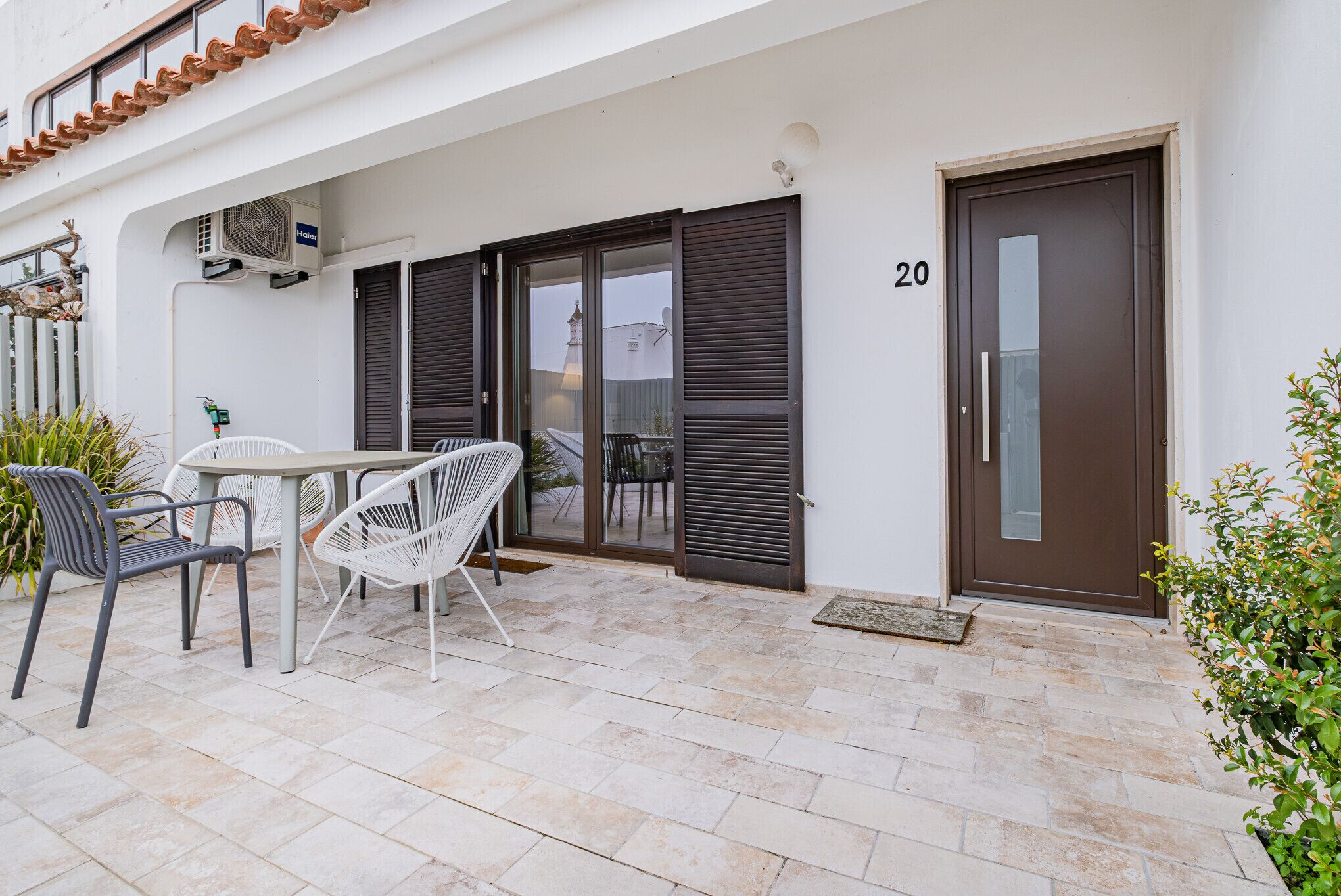 A patio with a table and chairs, a door with the number 20, and an air conditioning unit.