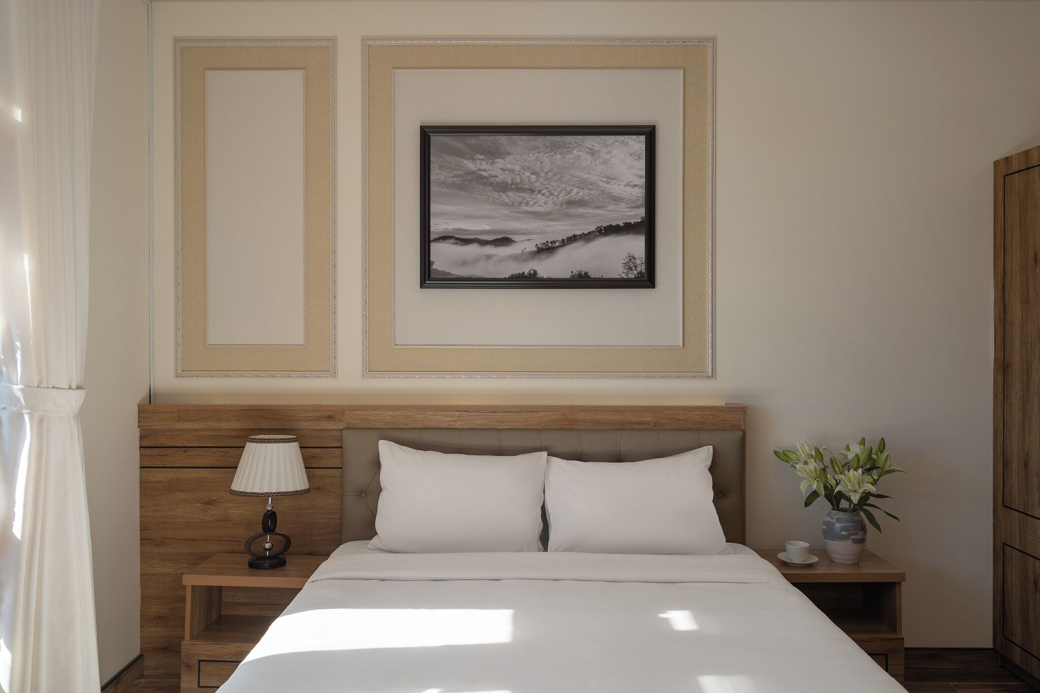 A neatly arranged hotel room with a bed, a nightstand with a lamp, a framed picture on the wall, and a small potted plant.