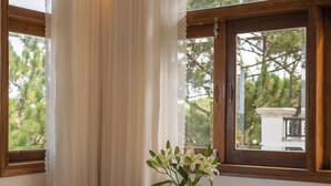 Una habitació amb taula blanca, dues cadires negres, un ram de flors i una finestra amb cortines.
