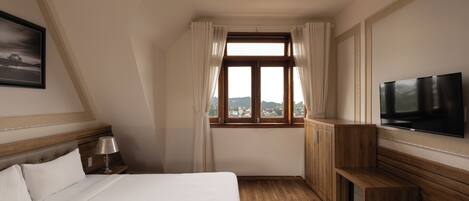 Habitación de hotel con cama, televisor, banca de madera, mesita de noche y ventana con cortinas.