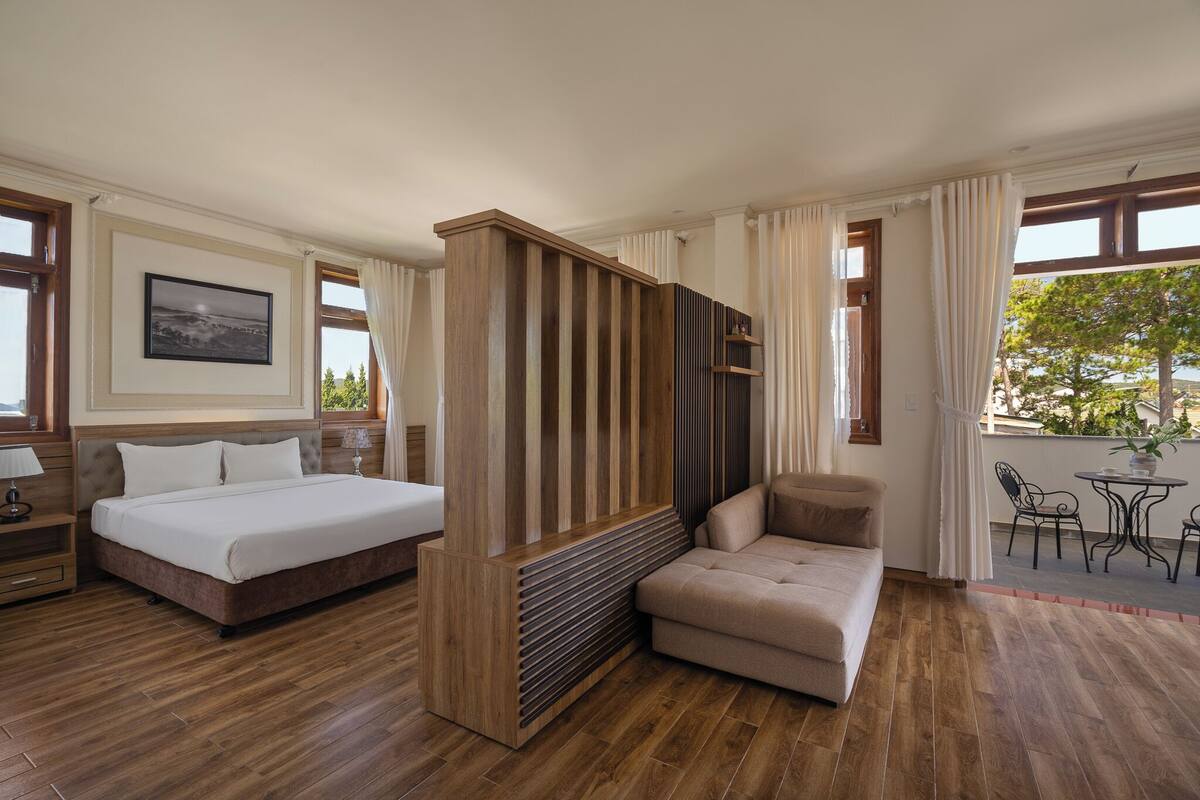 A hotel room with a bed, a sofa, a TV, and a dining area with chairs and a table.