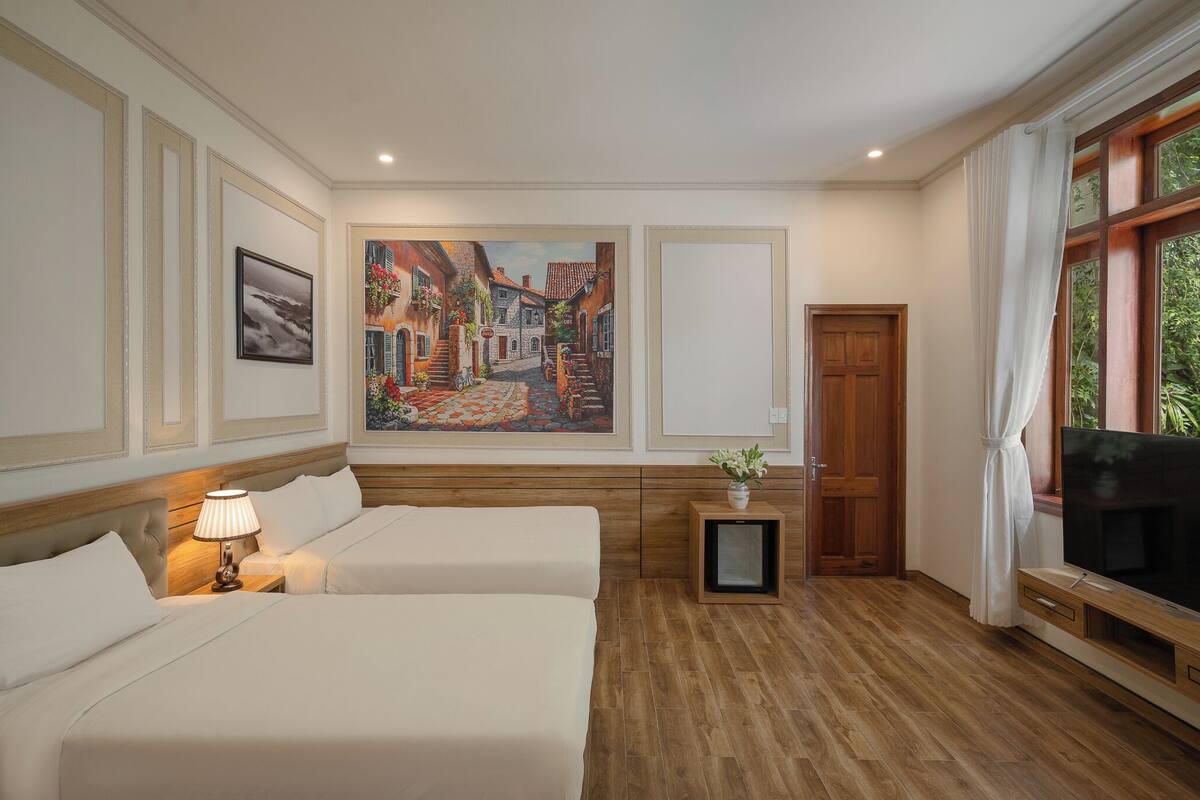 A hotel room with two beds, a painting on the wall, a TV, and a window with curtains.