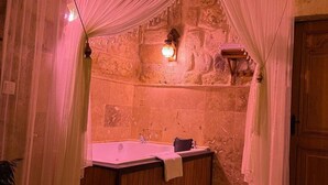 A stone-walled bathroom with a wooden bathtub, a towel, and a rug on the floor. - Songül Hanım Konağı (Ürgüp)