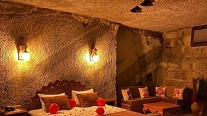 A cozy room with a stone wall, a bed with red balloons, a sofa, and a coffee table. - Songül Hanım Konağı (Ürgüp)