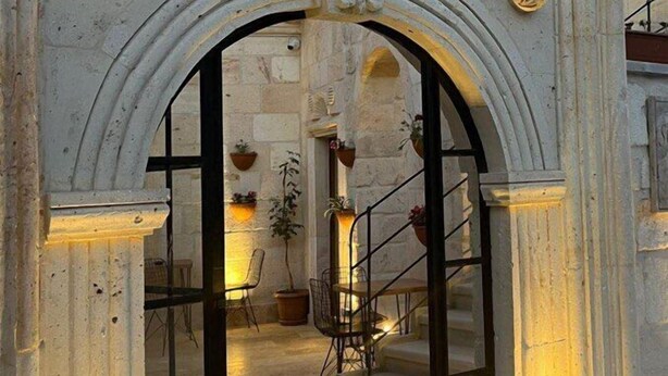 An ornate stone archway with a circular motif at the top, leading into a building with a staircase and potted plants. - Songül Hanım Konağı (Ürgüp)