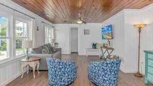A cozy room with wooden ceiling, a gray sofa, two blue patterned ottomans, a small white table, a floor lamp, and a painting on the wall. - 3 Blocks to Beach + FREE Golf Cart | Sleeps 10 (North Myrtle Beach)