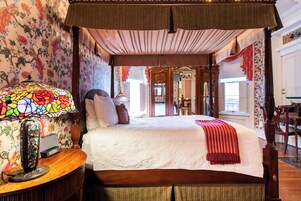 Un dormitorio con cama a dosel, papel tapiz floral y una lámpara de vitral.