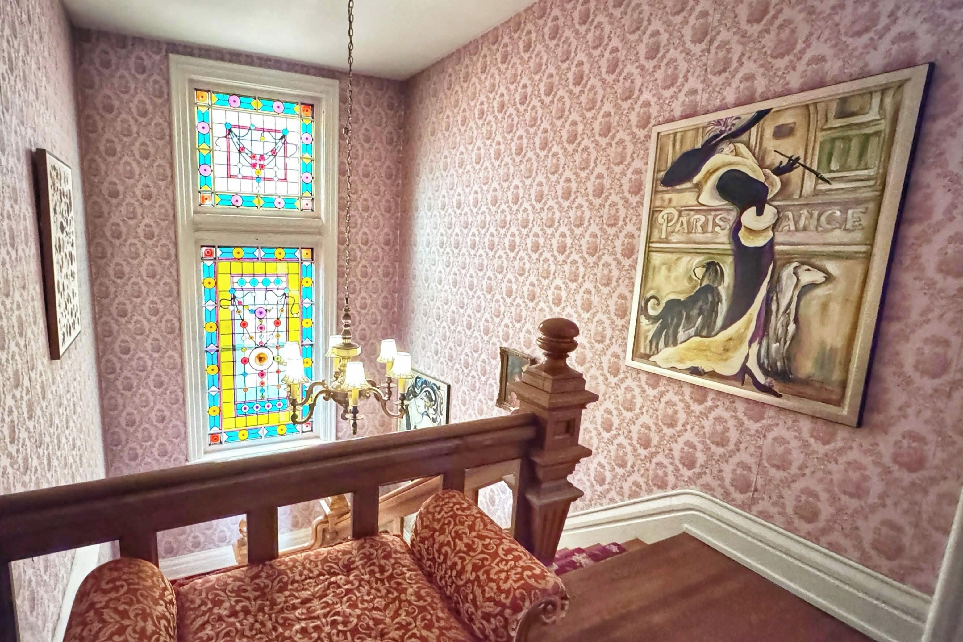 Un escalier orné d’un mur à motifs, une fenêtre à vitraux et un tableau représentant une femme avec un chien.