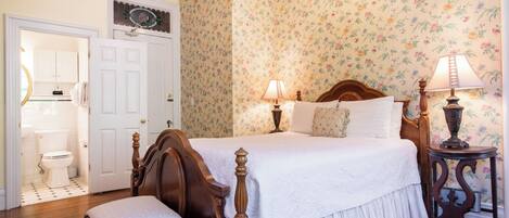 Une chambre à coucher avec un lit en bois, deux lampes de chevet, une chaise, une table de chevet et un papier peint à motifs floraux.
