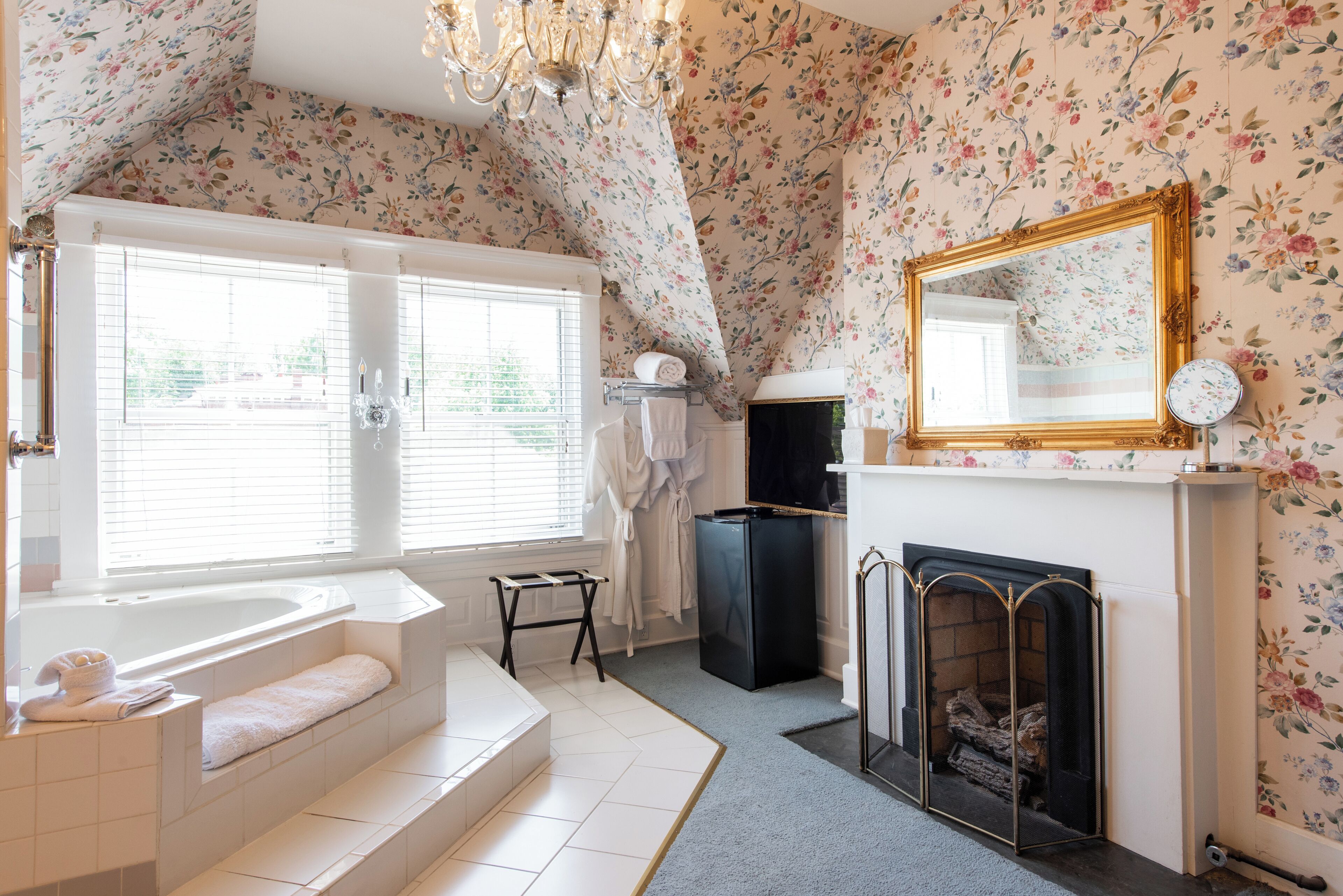 Une salle de bain avec une baignoire, un miroir, une cheminée et un papier peint à motifs floraux.