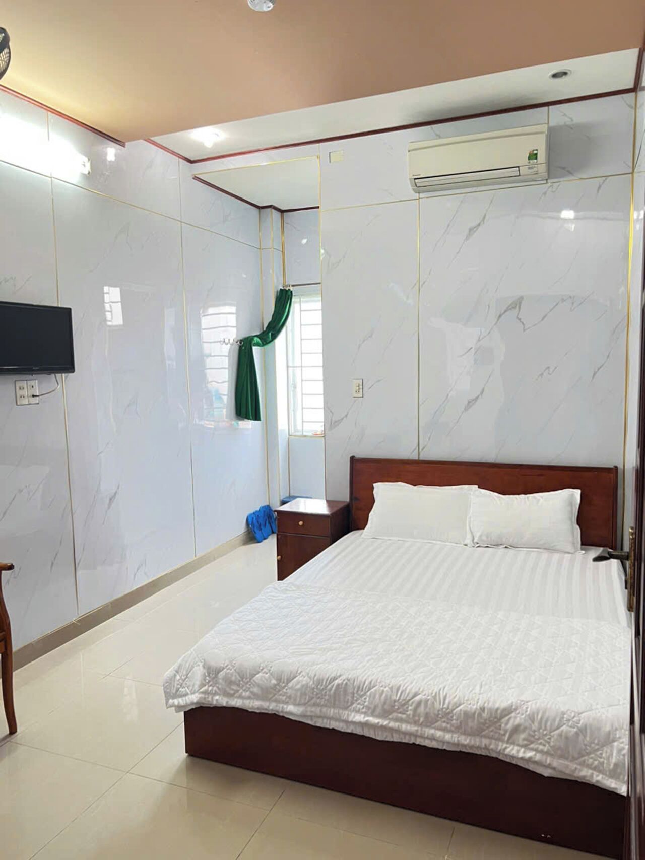 A hotel room with a large bed, a flat-screen TV mounted on the wall, and a window with a green curtain.